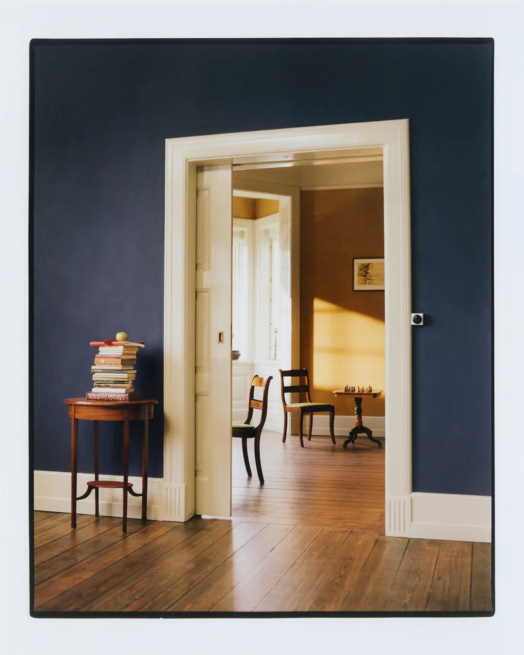 A dark blue Villa Hesnæs room looking through a doorway toward a chess table.