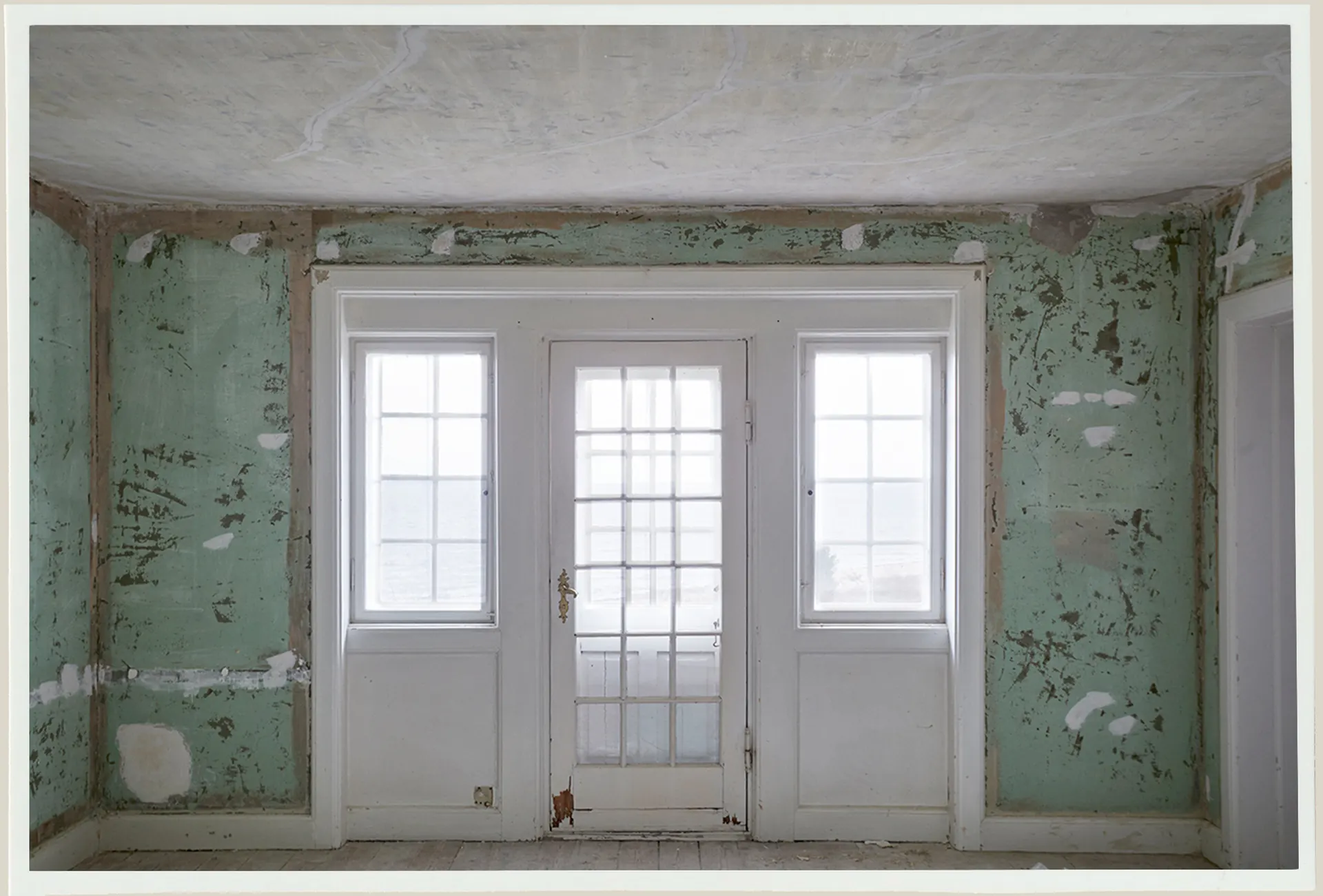A room with green worn walls and three white doors before restoration.