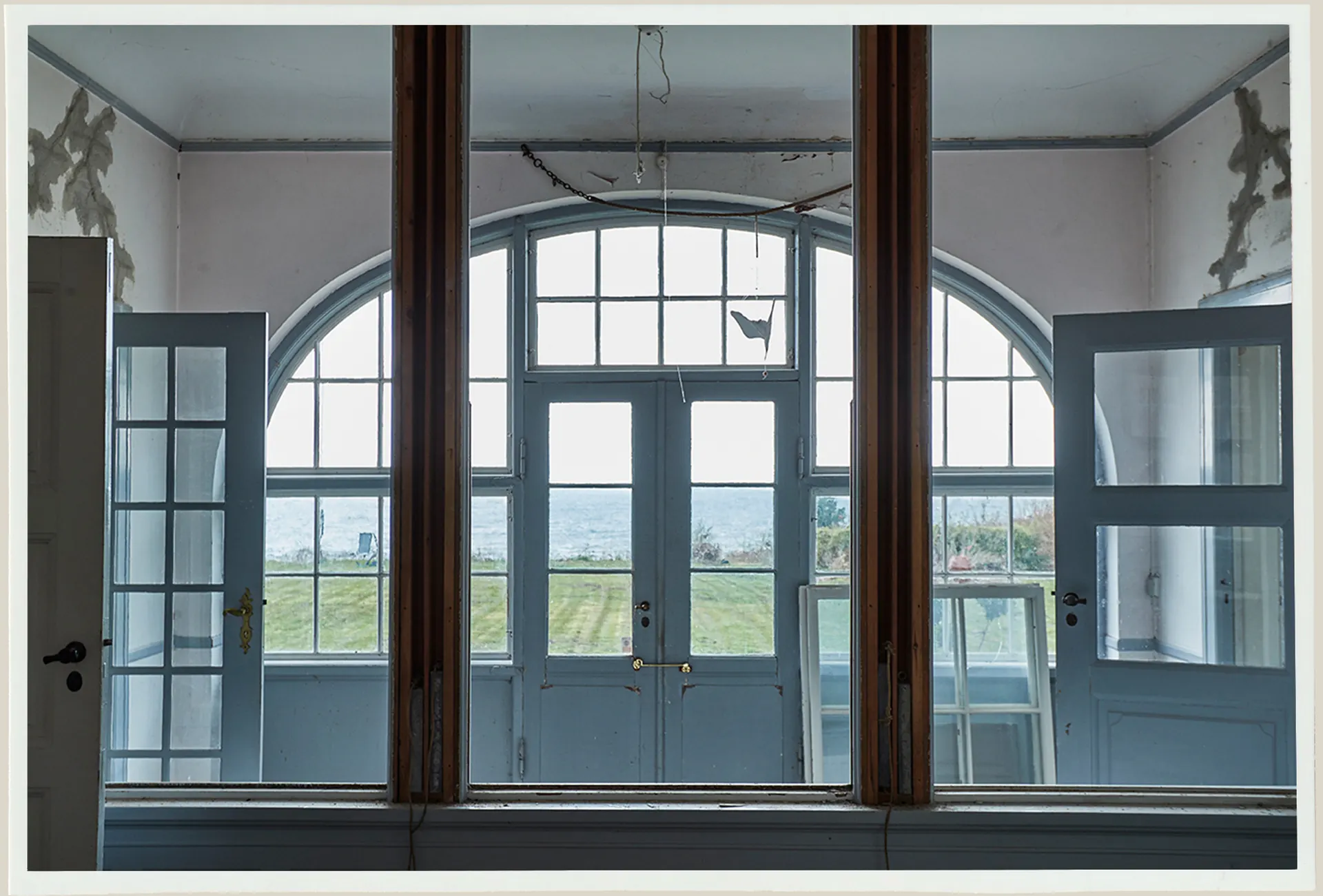 A restored arched window and blue doors looking out toward the sea.