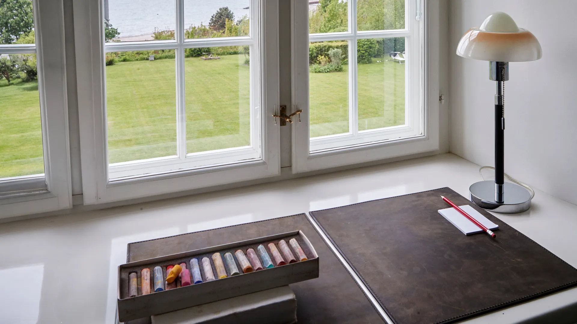 An artist workspace by a window overlooking the Villa Hesnæs garden and sea.