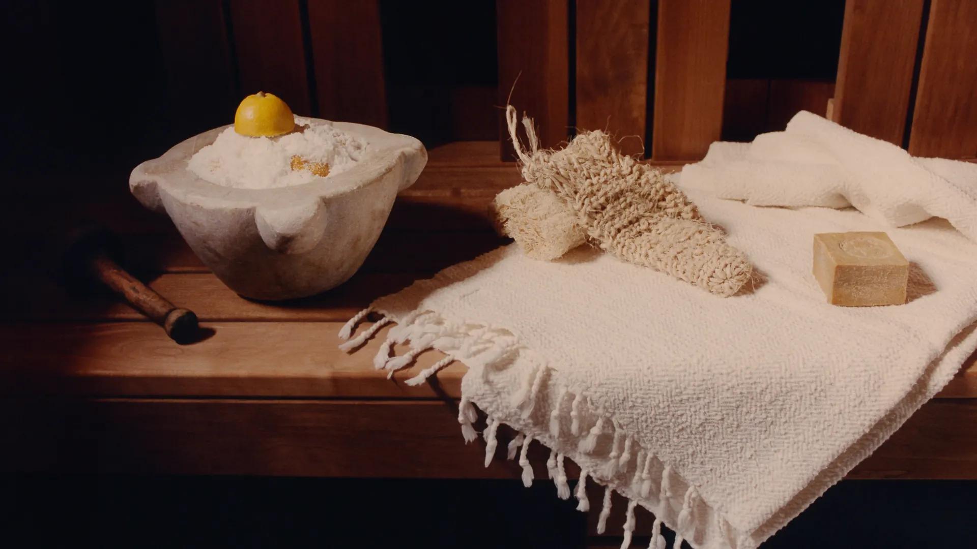 Sauna towels, salt, and wellness tools arranged on a wooden sauna bench.
